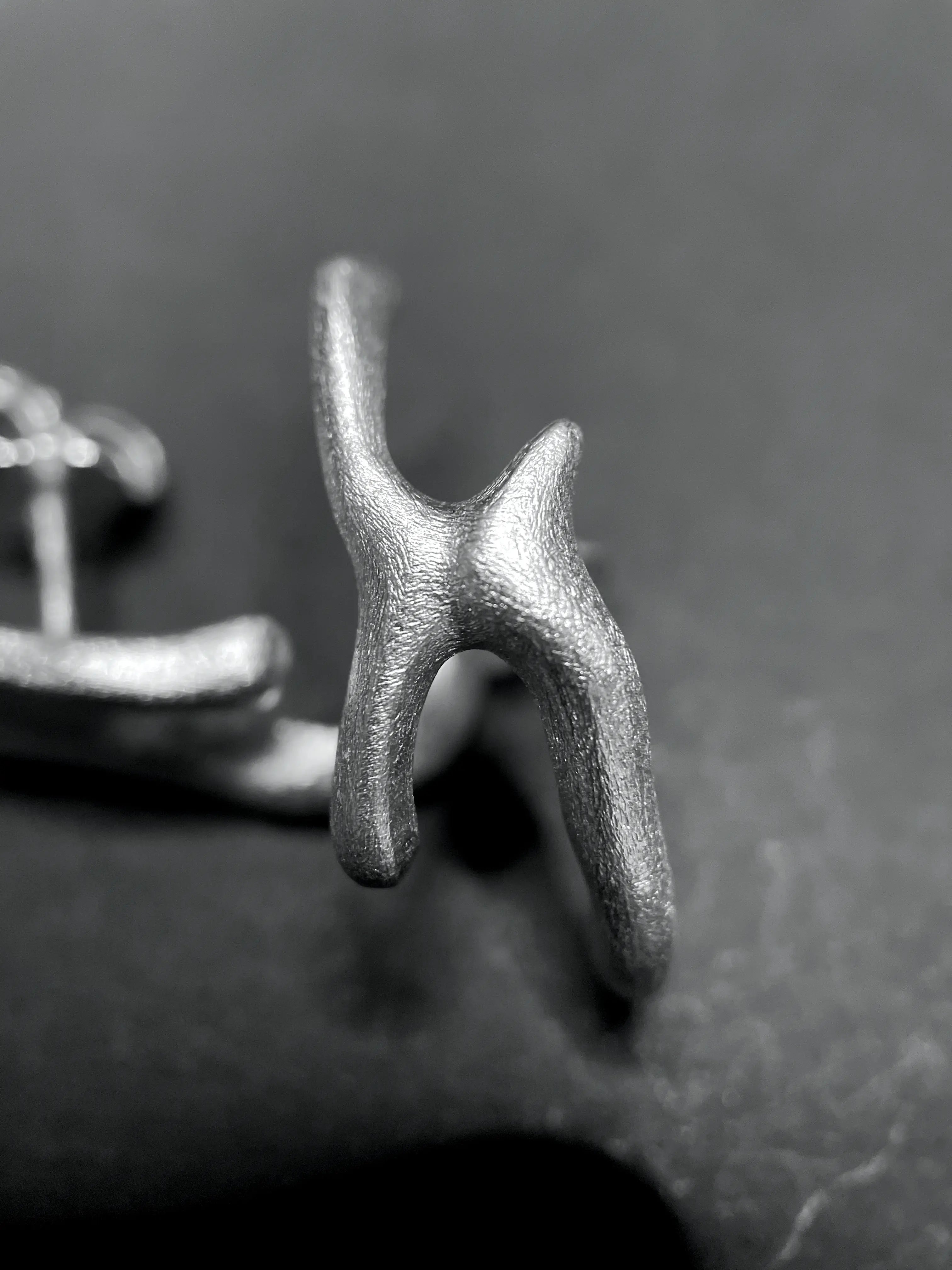 Gros plan d'une main tenant ou montrant une boucle d'oreille Arki en argent. Détail du travail fait main.