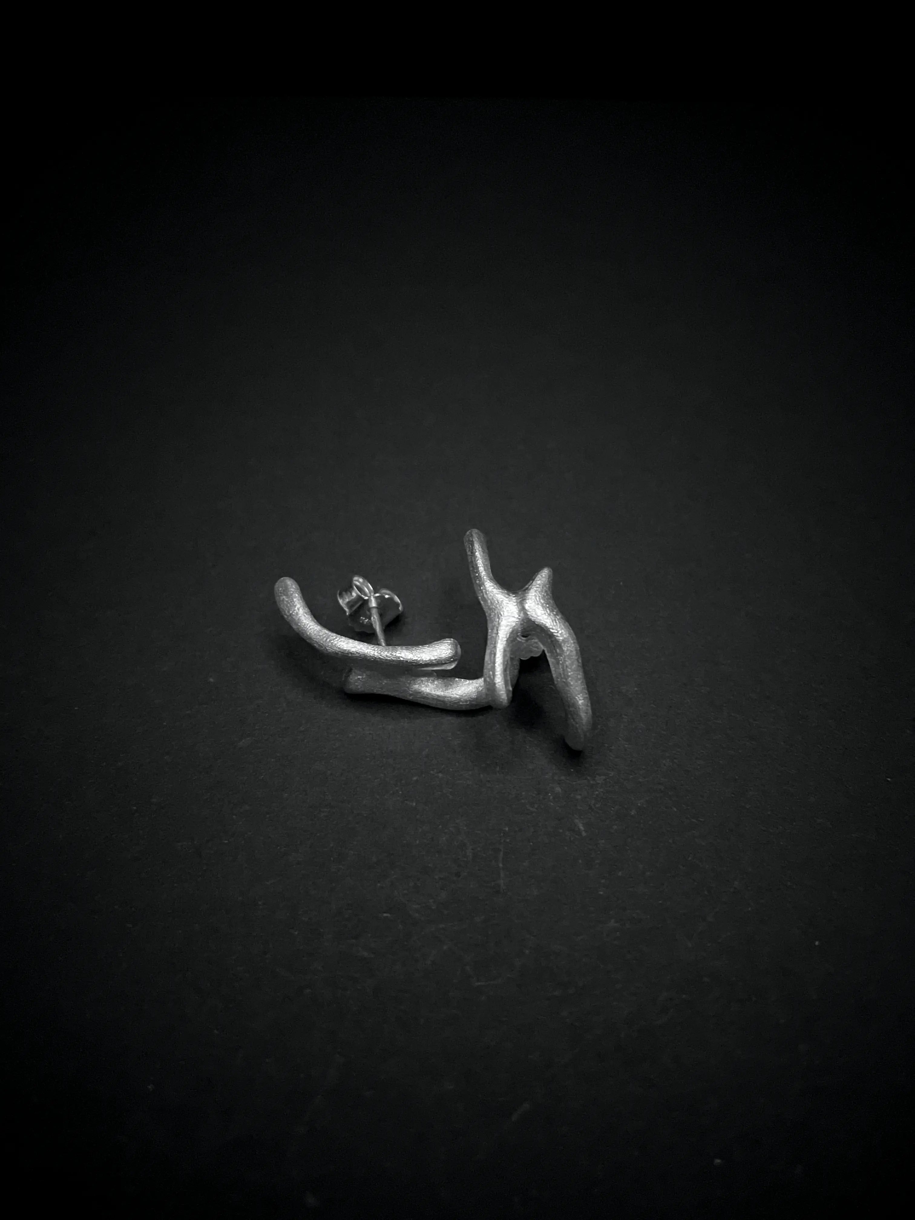 Photo minimaliste d'une boucle d'oreille Arki en argent 925 sur fond noir, vue de loin.