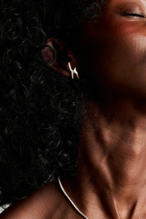 Portrait d'une femme portant la boucle d'oreille Arki en argent 925, vue de côté. Bijou artisanal français.