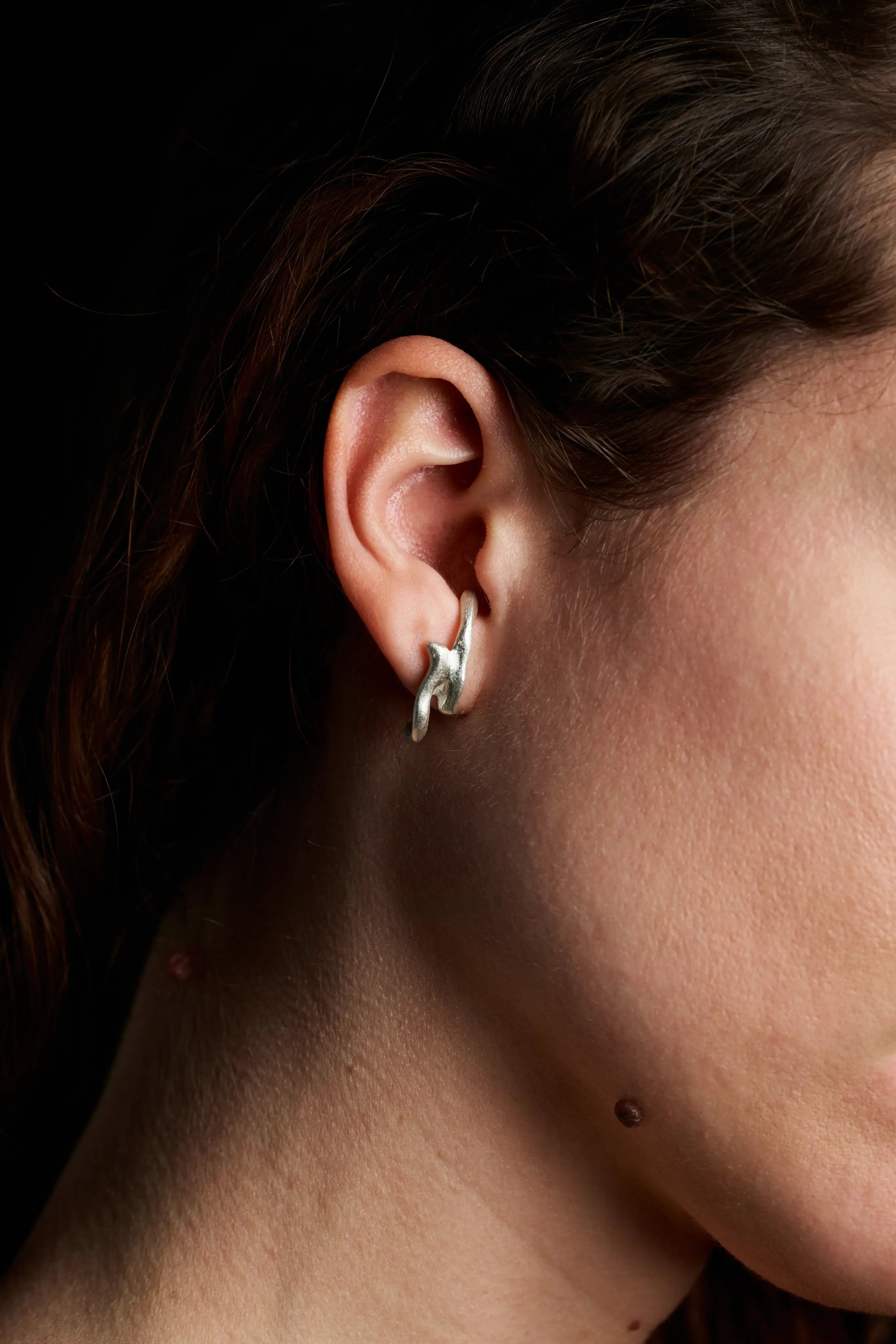 Portrait d'une femme portant la boucle d'oreille Arki en argent 925, vue de côté. Bijou artisanal français.