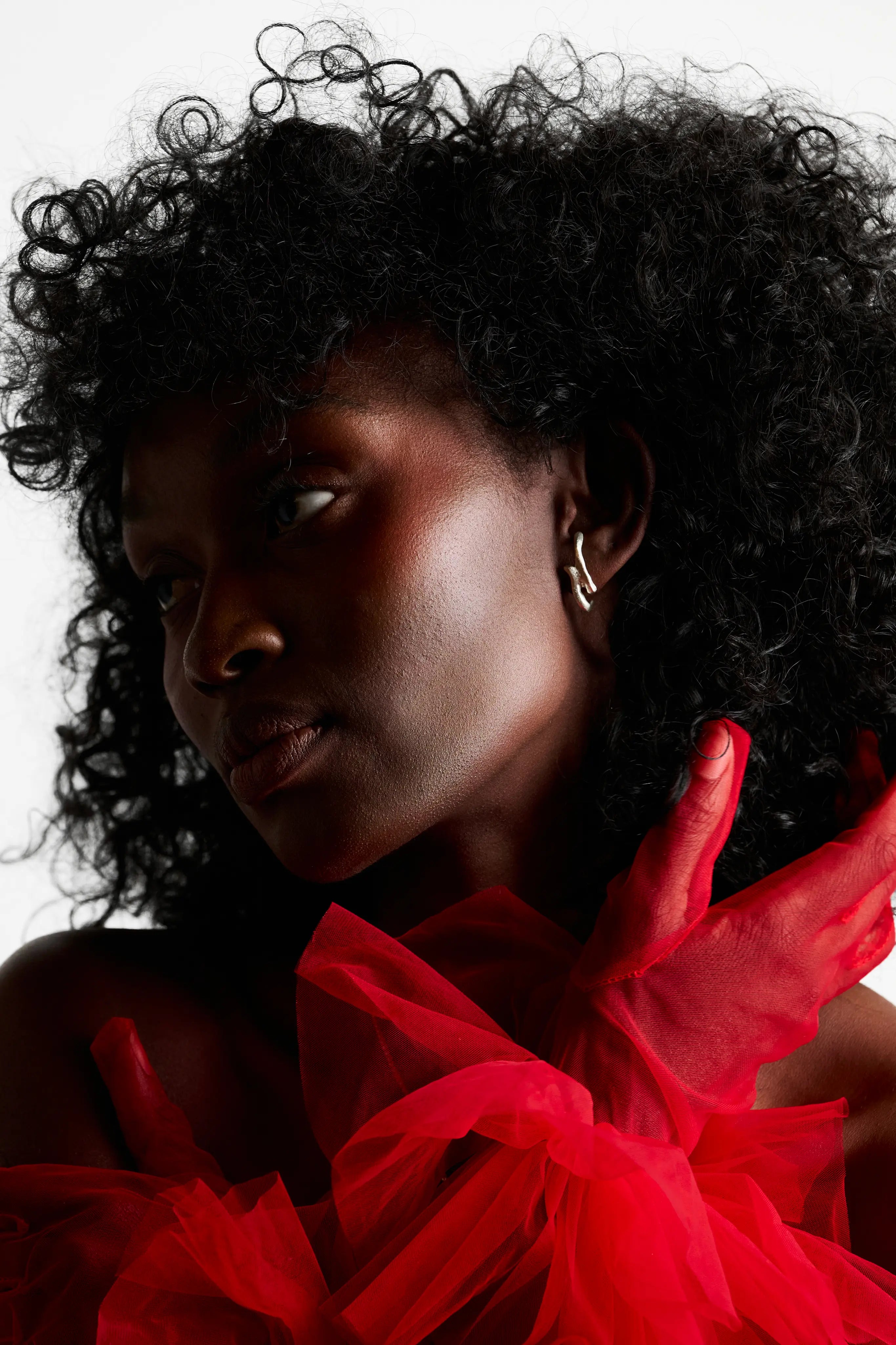 Portrait d'une femme portant les boucles d'oreilles Arki en argent 925, avec un voile rouge. Bijou fait main éthique.
