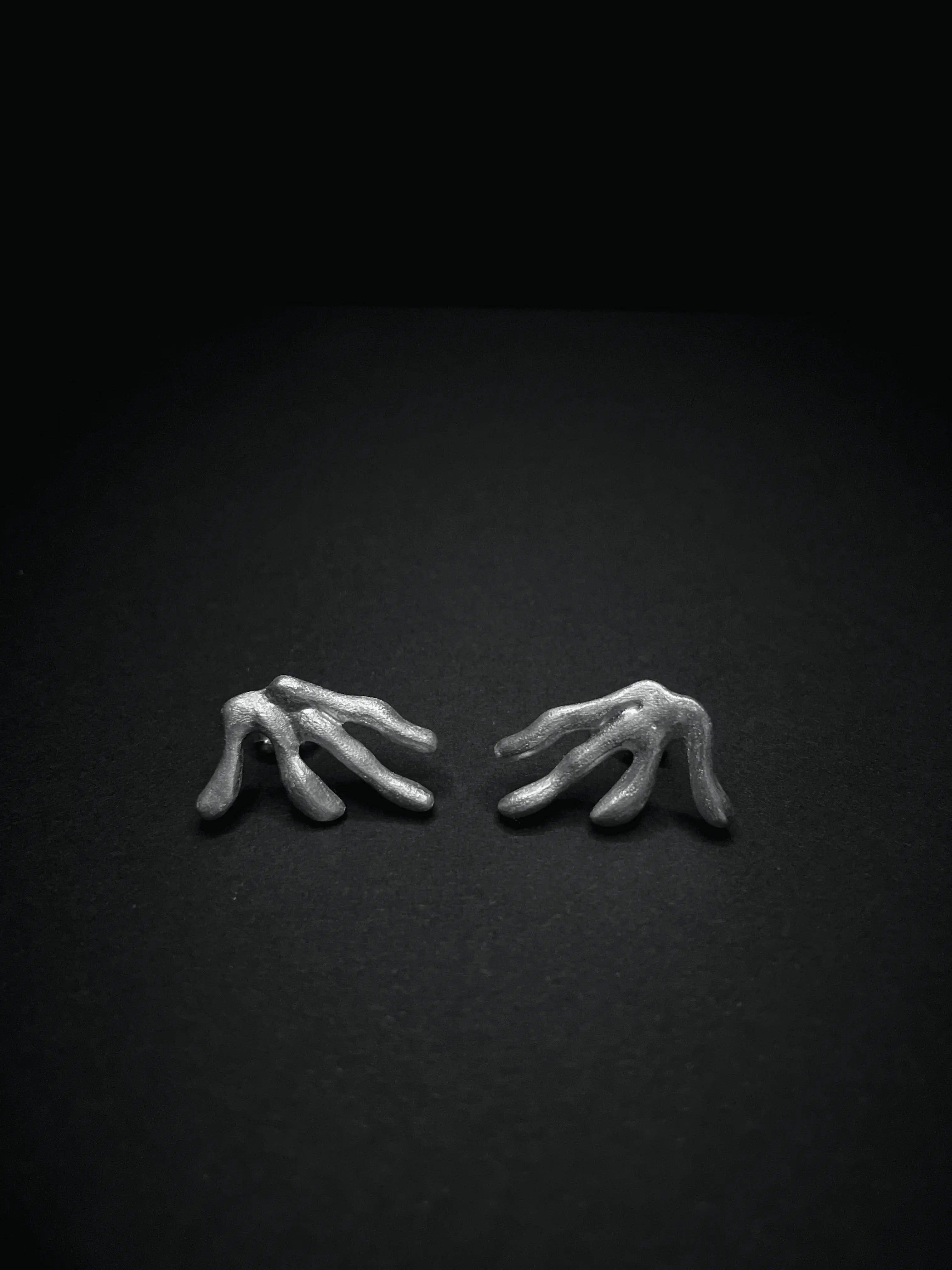 Les boucles d'oreilles Ména en argent, design abstrait, sur un fond sombre. Collection Corail Synonys.