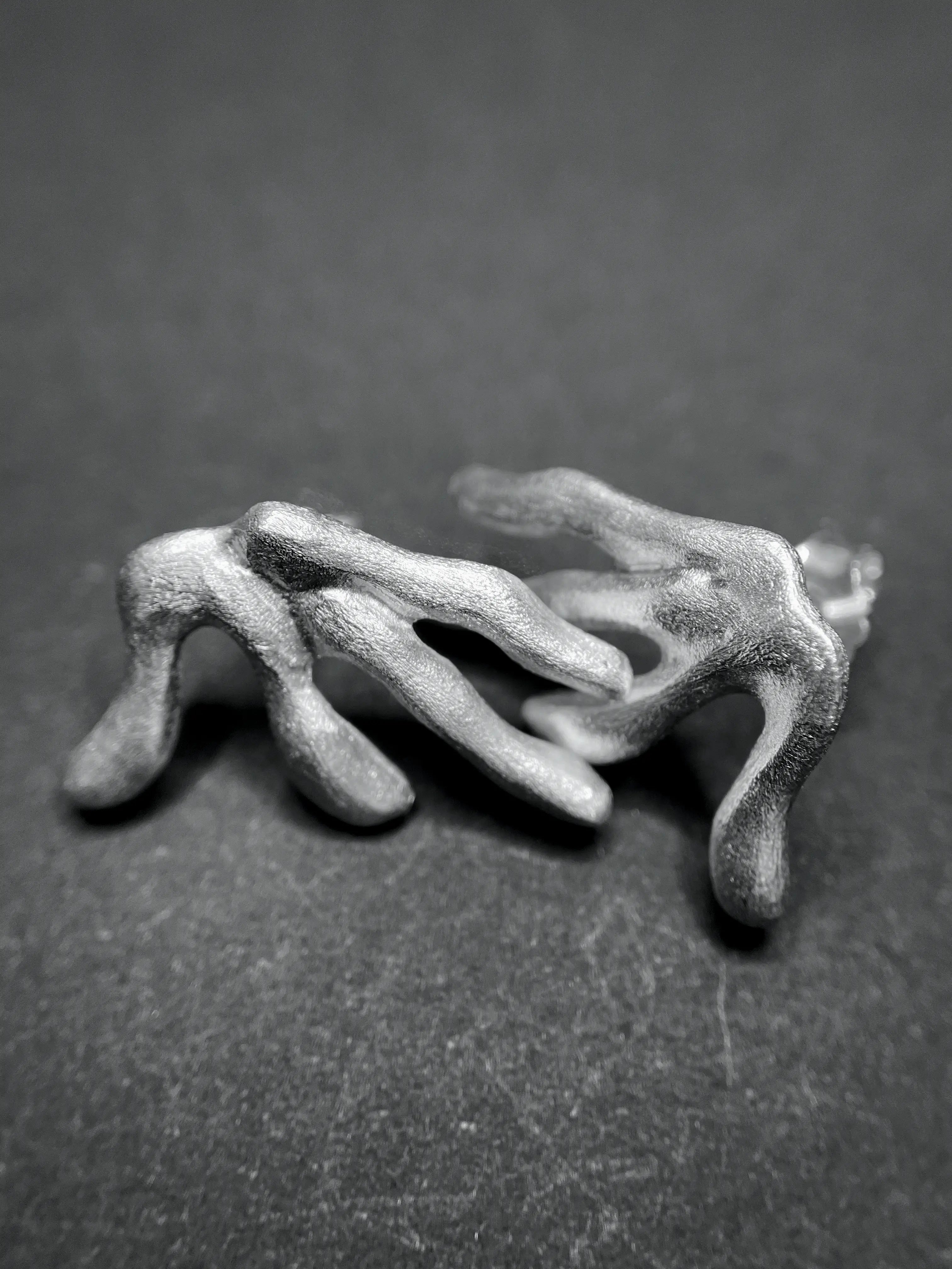 Macro des boucles d'oreilles Ména tenues par une main, montrant la texture et le travail artisanal.