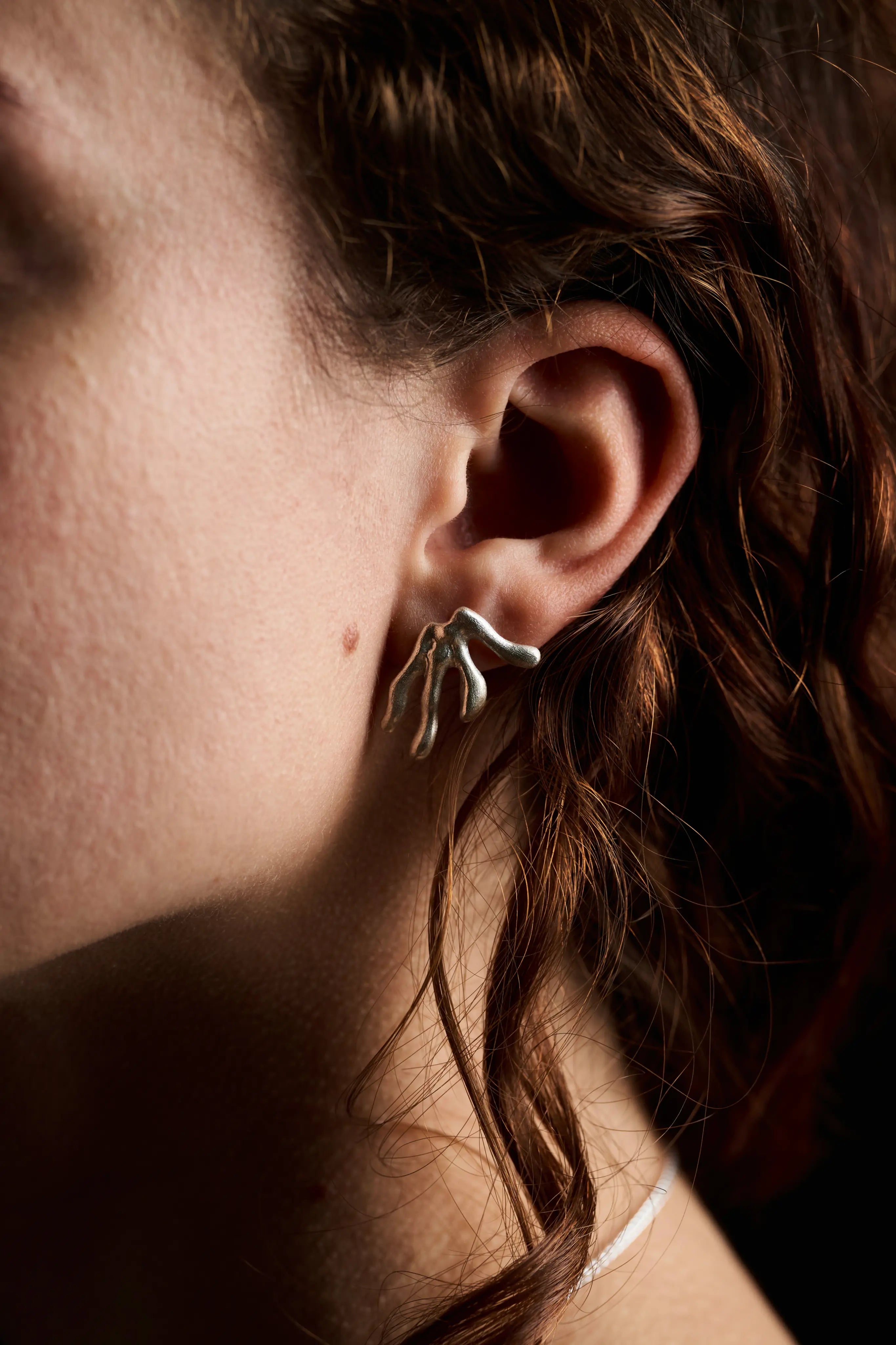 Gros plan sur le profil d'une femme portant la boucle d'oreille Ména en argent. Fait main en France.