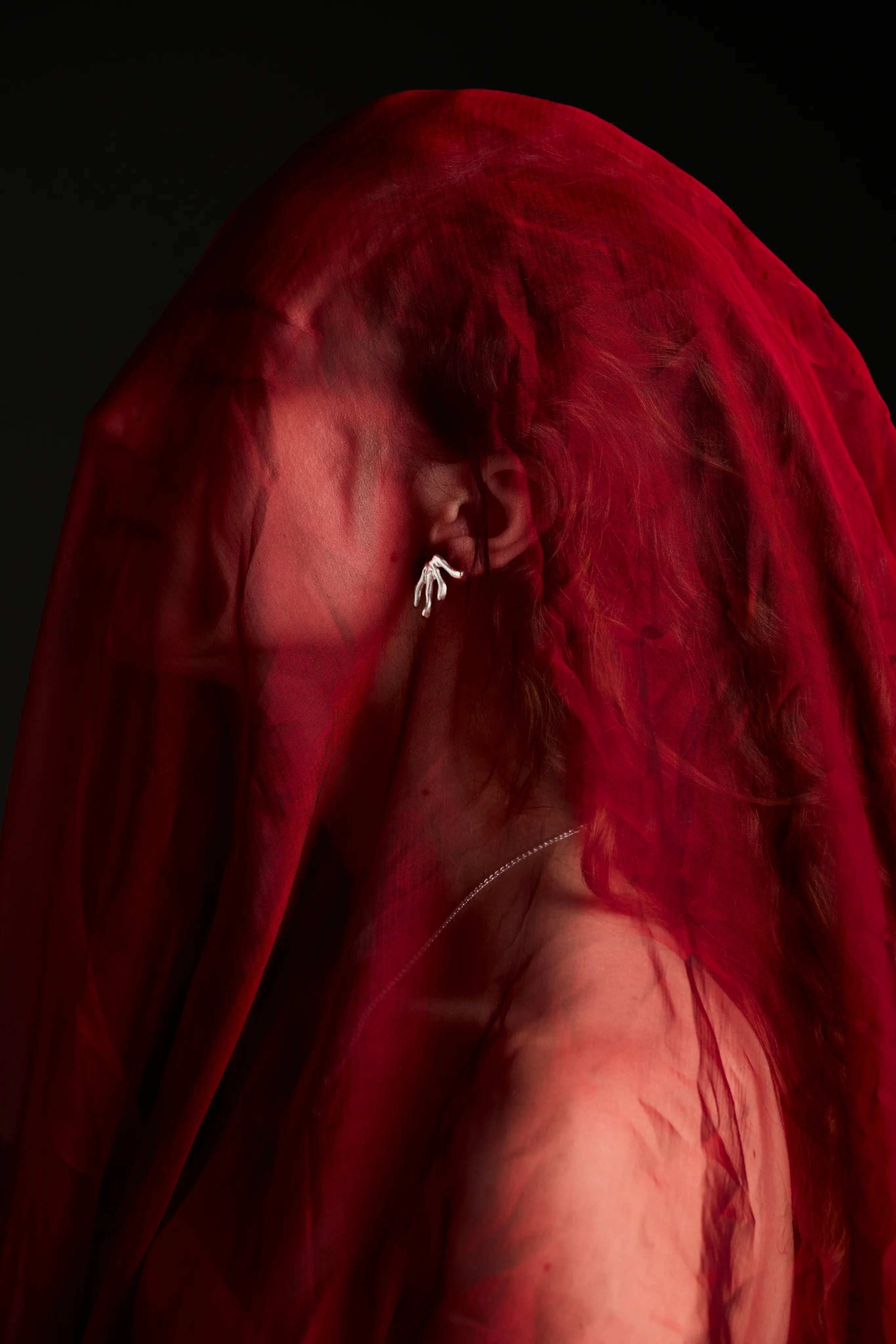 Boucle d'oreille Mena Synonys en argent 925, portée sur une femme voilée de rouge. Bijou artisanal, collection Corail.