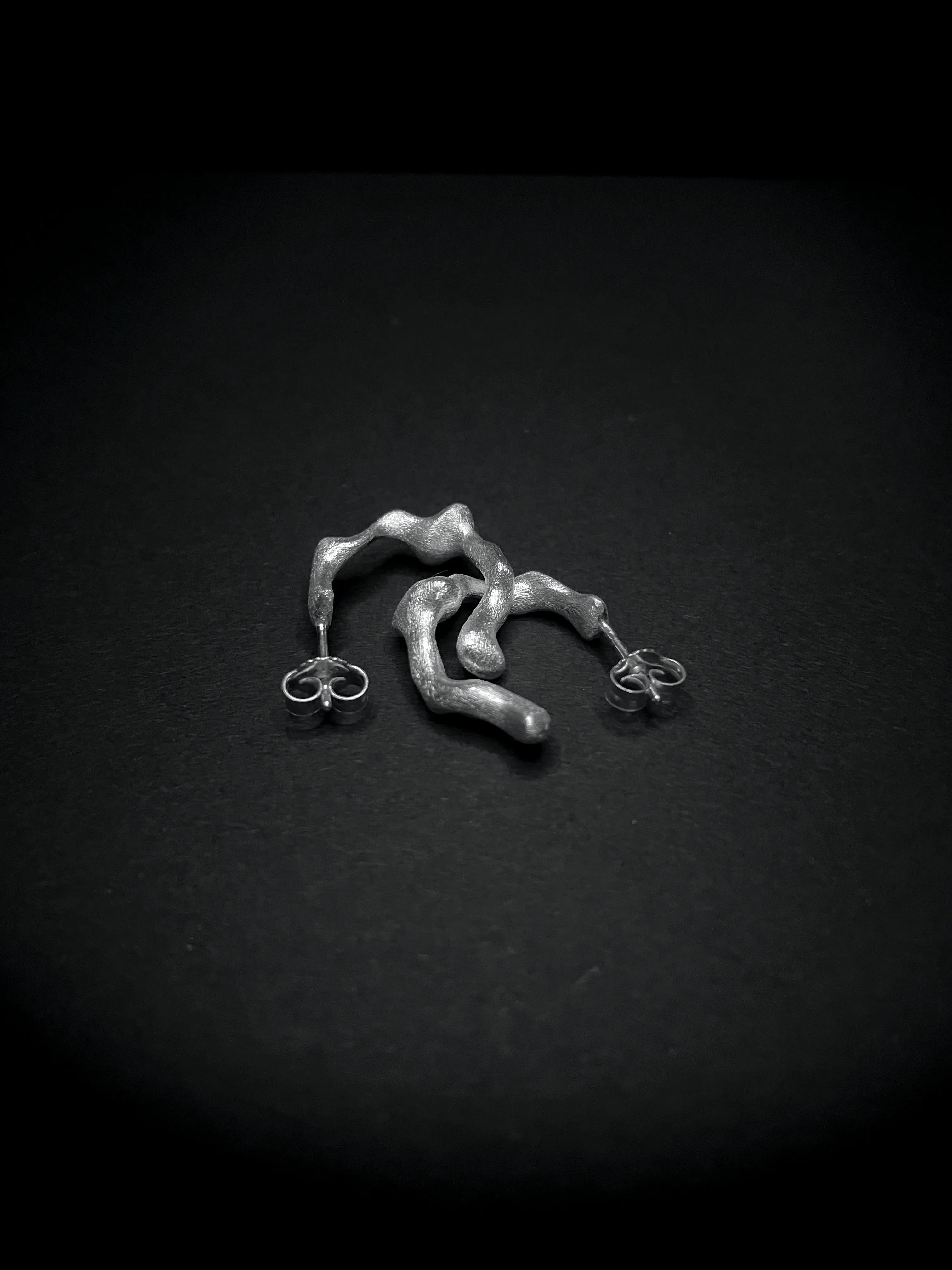 Détail des boucles d'oreilles Spira en argent, design organique, sur fond noir. Collection Corail.
