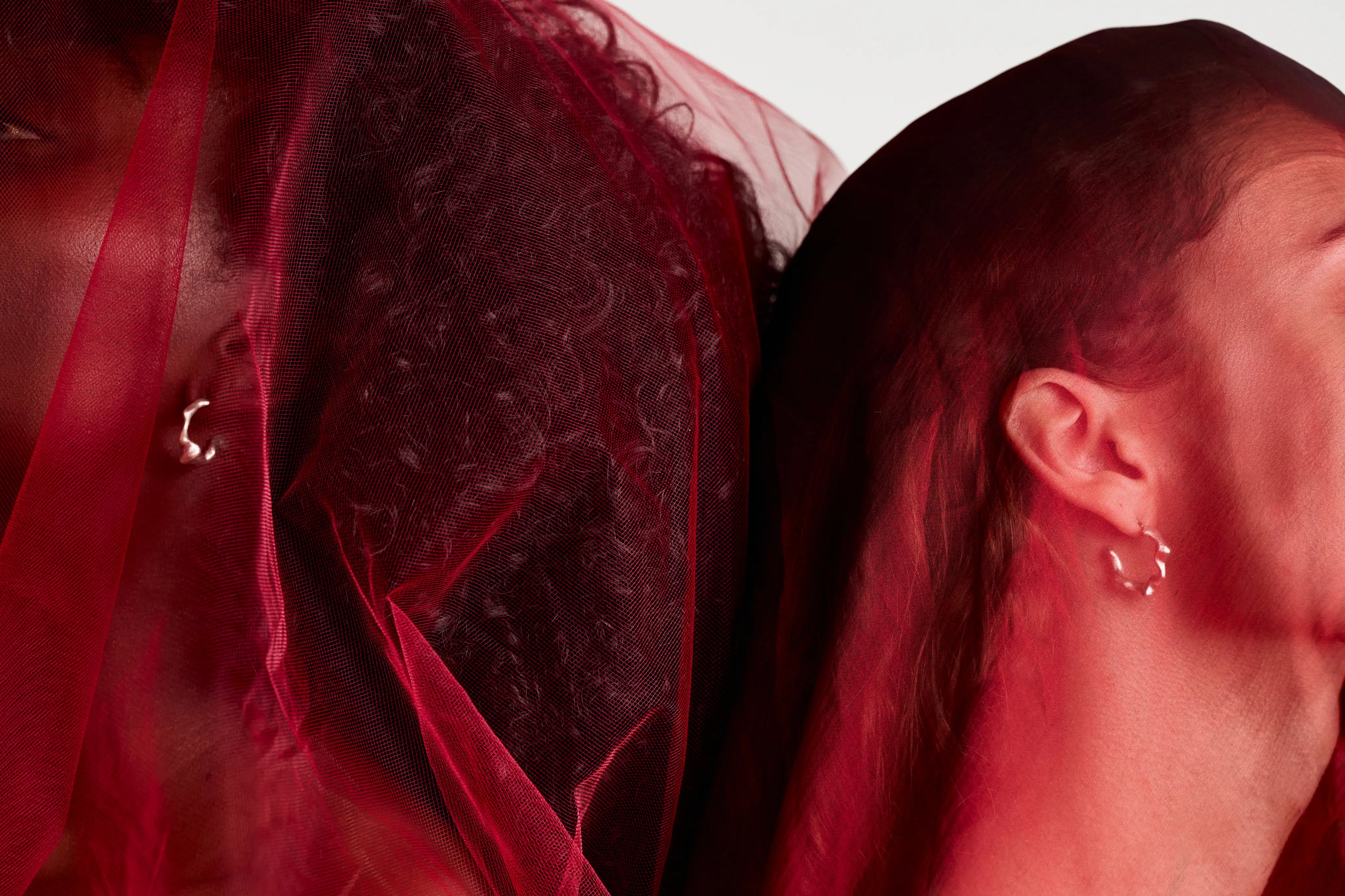 Boucles d'oreilles Spira Synonys en argent, portées par deux femmes avec un voile rouge. Bijoux artisanaux éthiques.