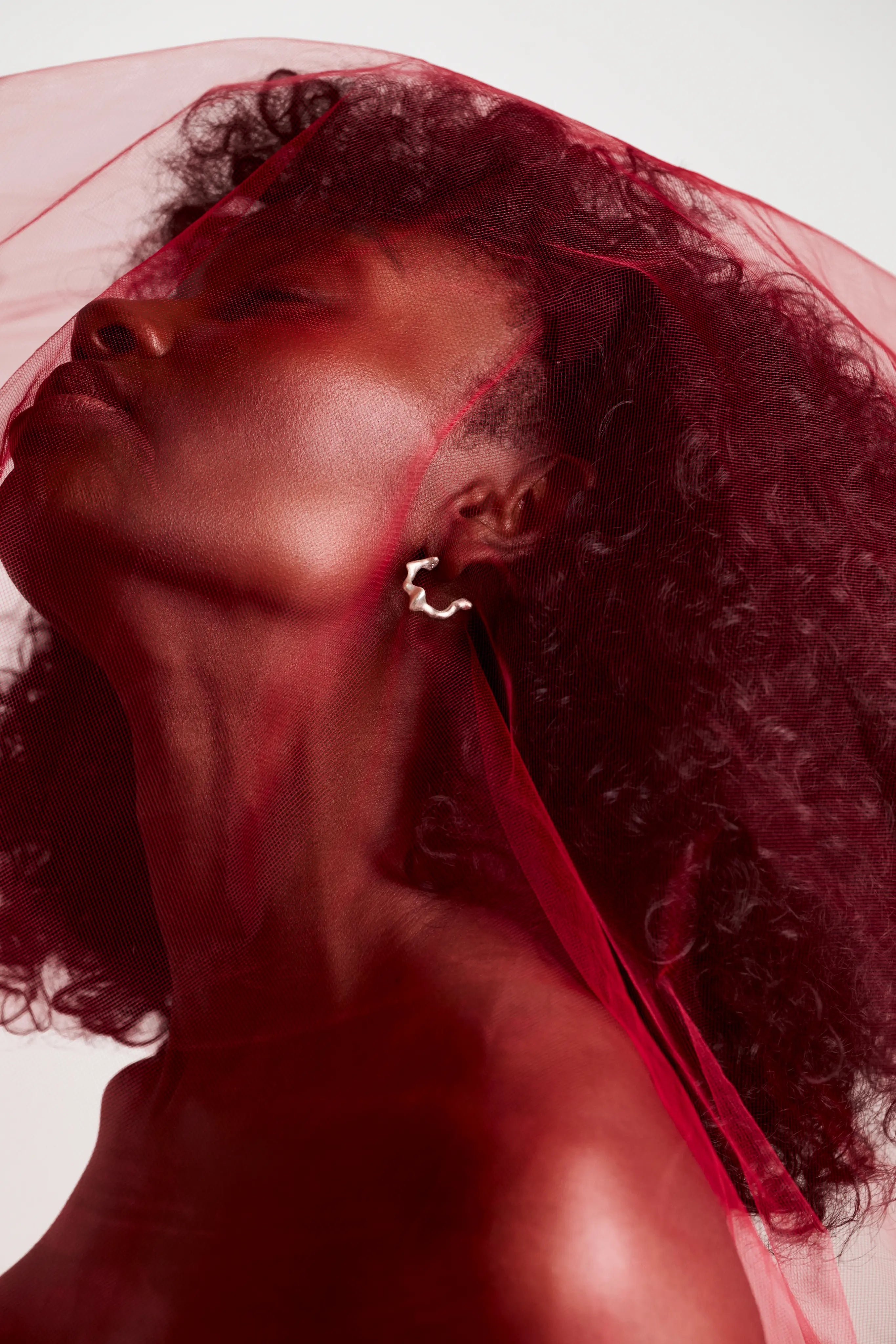 Boucle d'oreille Spira Synonys en argent 925, portée sur une femme voilée de rouge. Bijou artisanal, collection Corail.