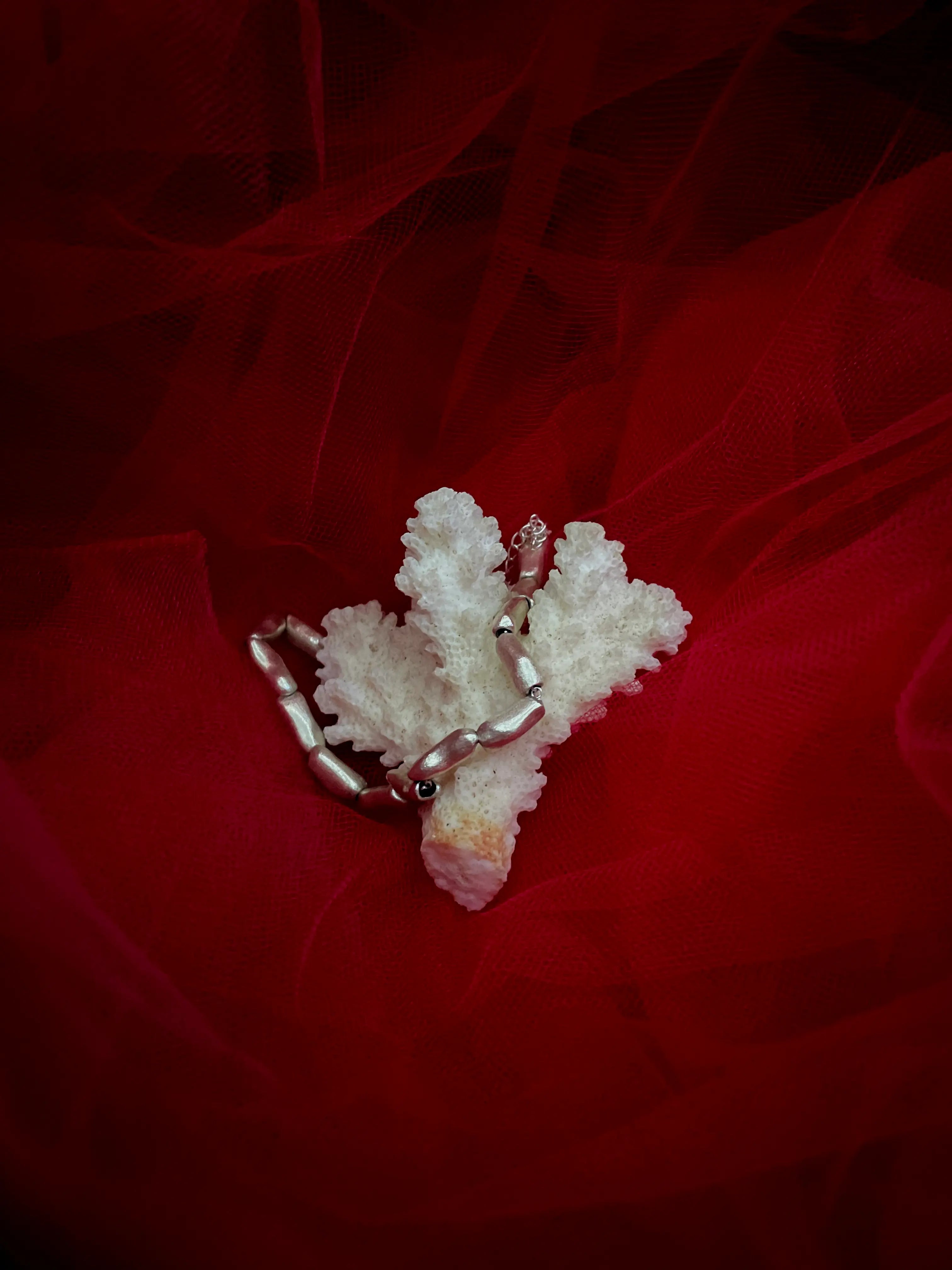 Collier Fracta Synonys en argent 925 avec perles d'argent, posé sur du corail blanc et tissu rouge. Bijou fait main, collection Corail.