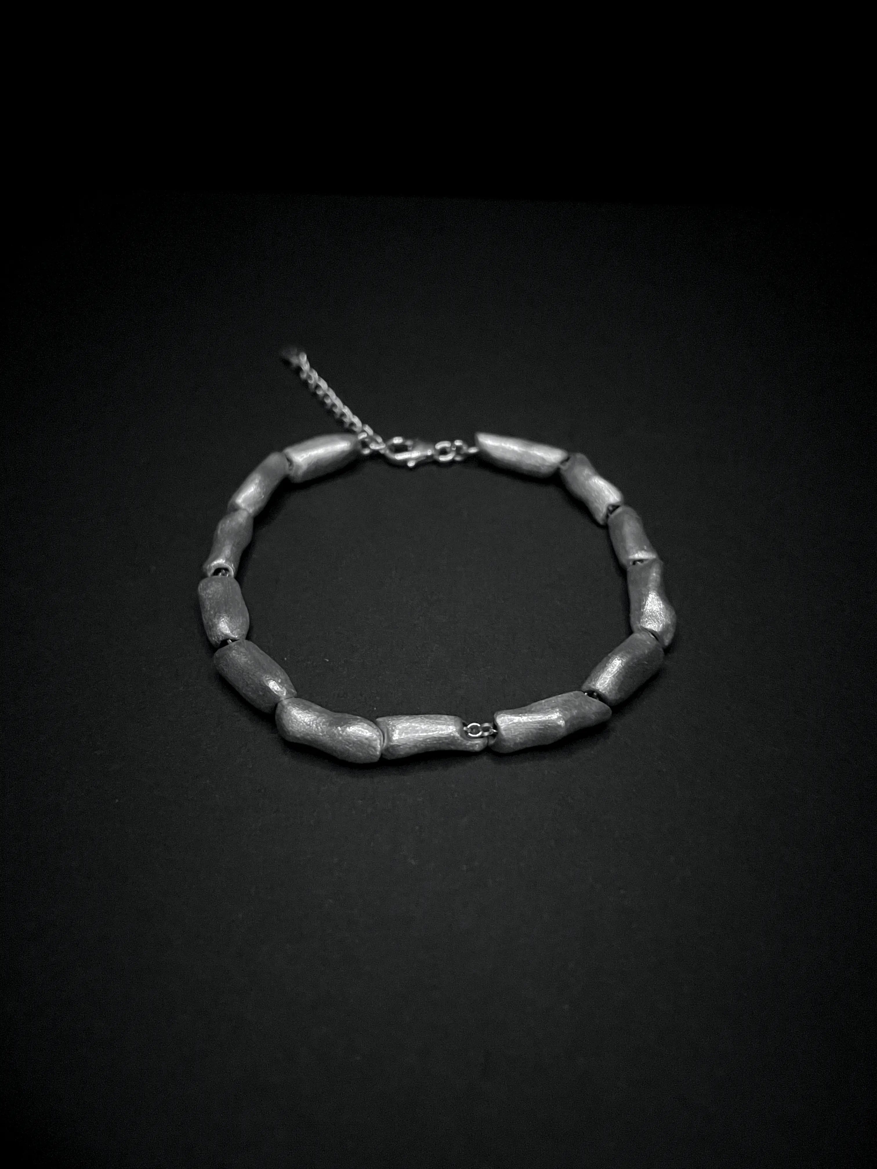 Gros plan sur les perles d'argent texturées du bracelet Fracta sur fond sombre.