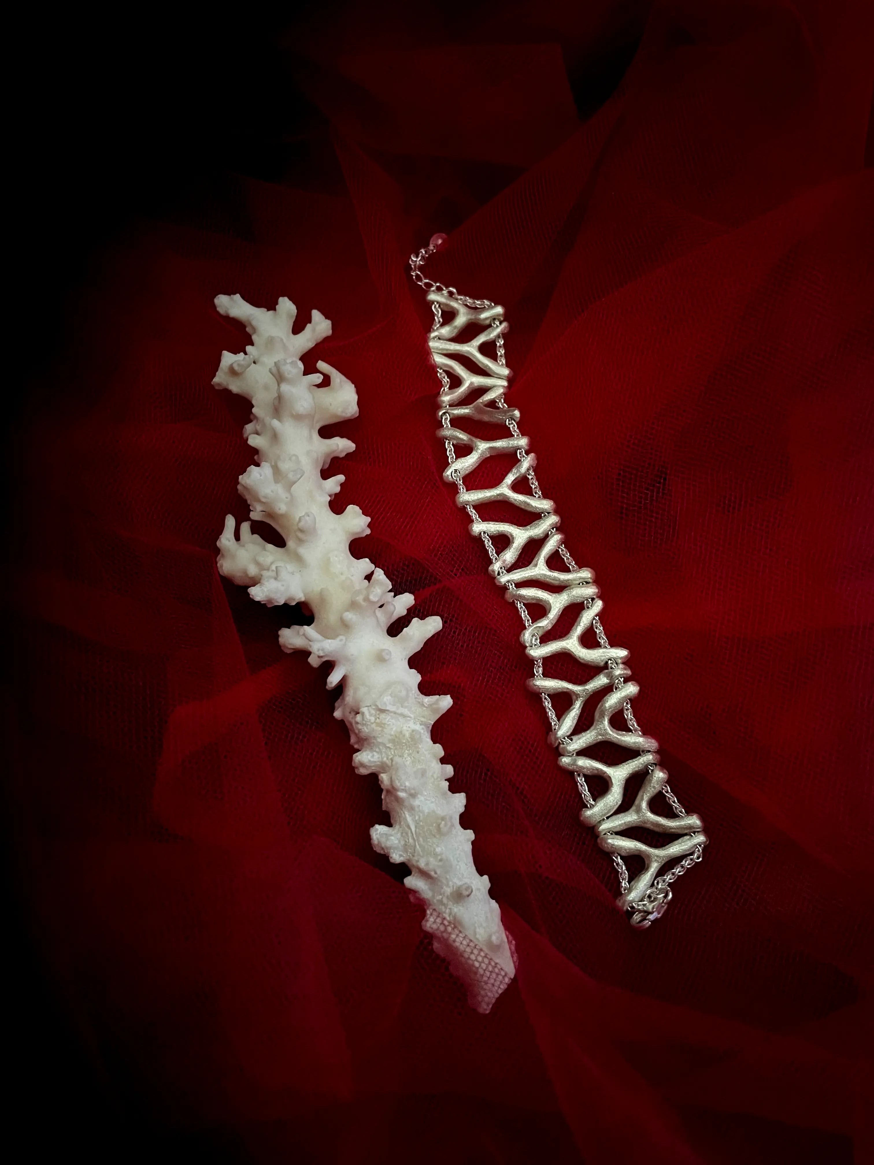 Bracelets Isopora en argent à côté d'un corail sur fond rouge. Bijoux faits main Synonys.