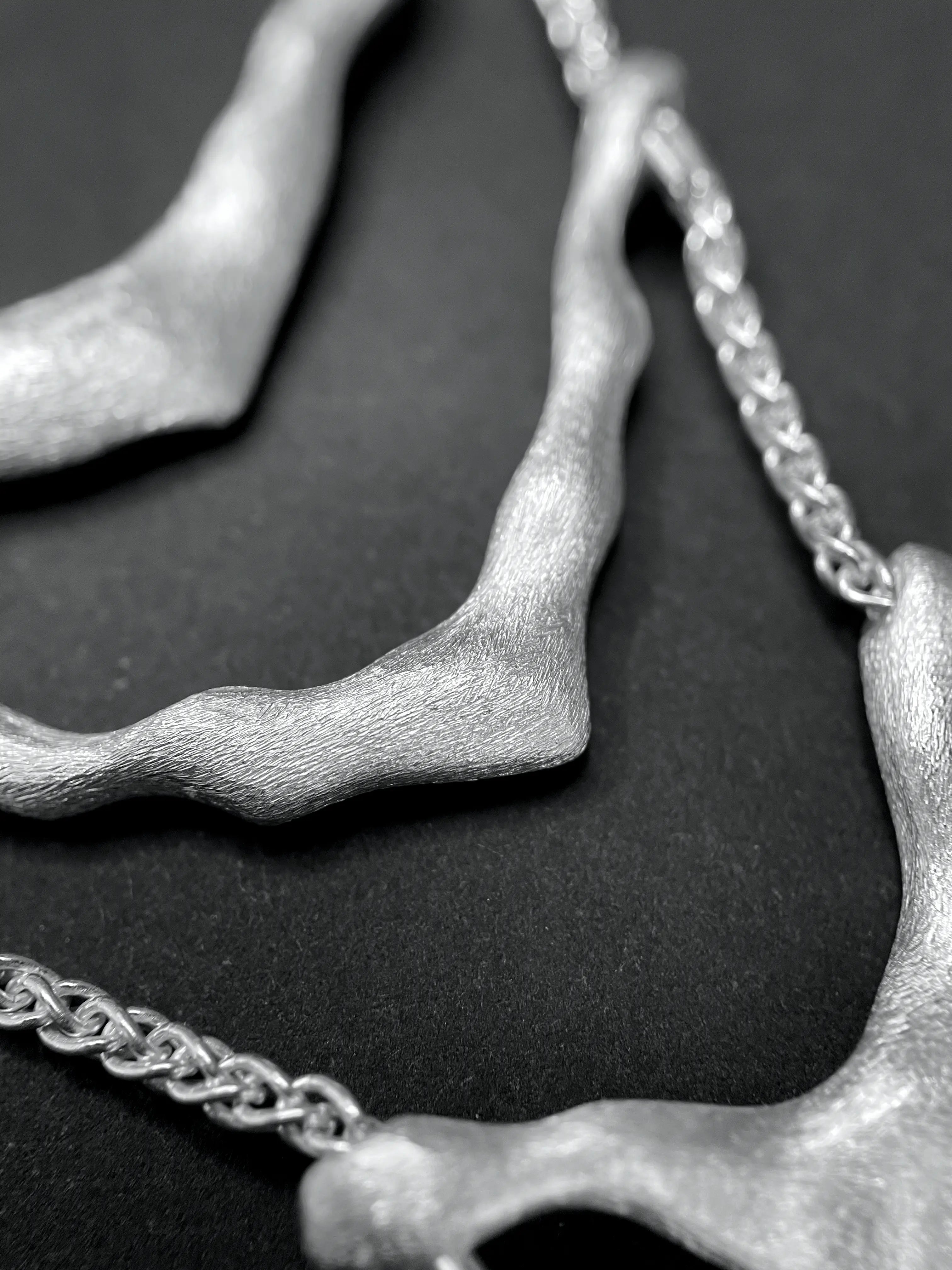 Macro du pendentif du collier de dos Exo, montrant la texture et le travail artisanal.