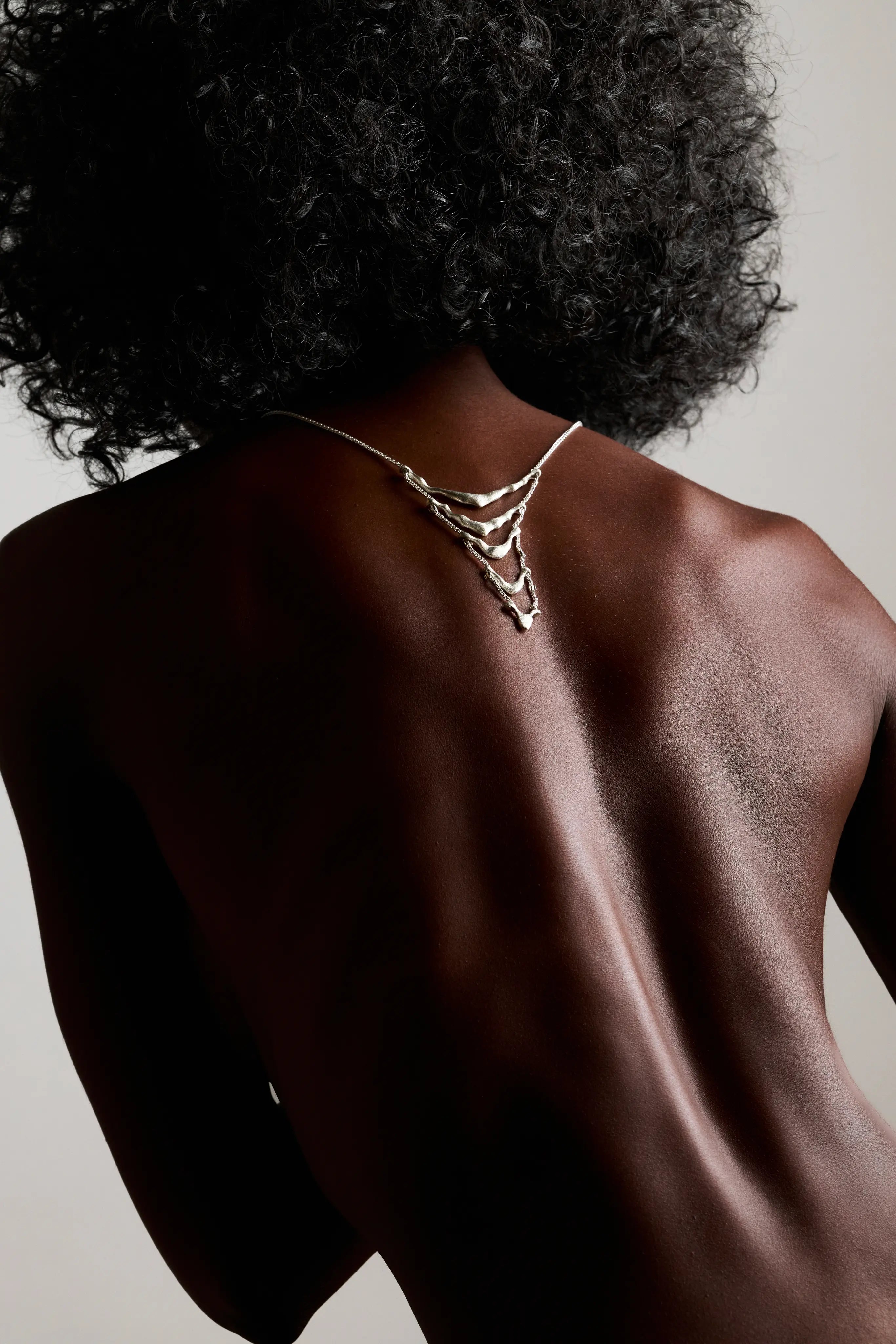 Collier de dos Exo Synonys en argent 925, vu de dos, sur une femme aux cheveux bouclés. Bijou fait main, collection Corail.