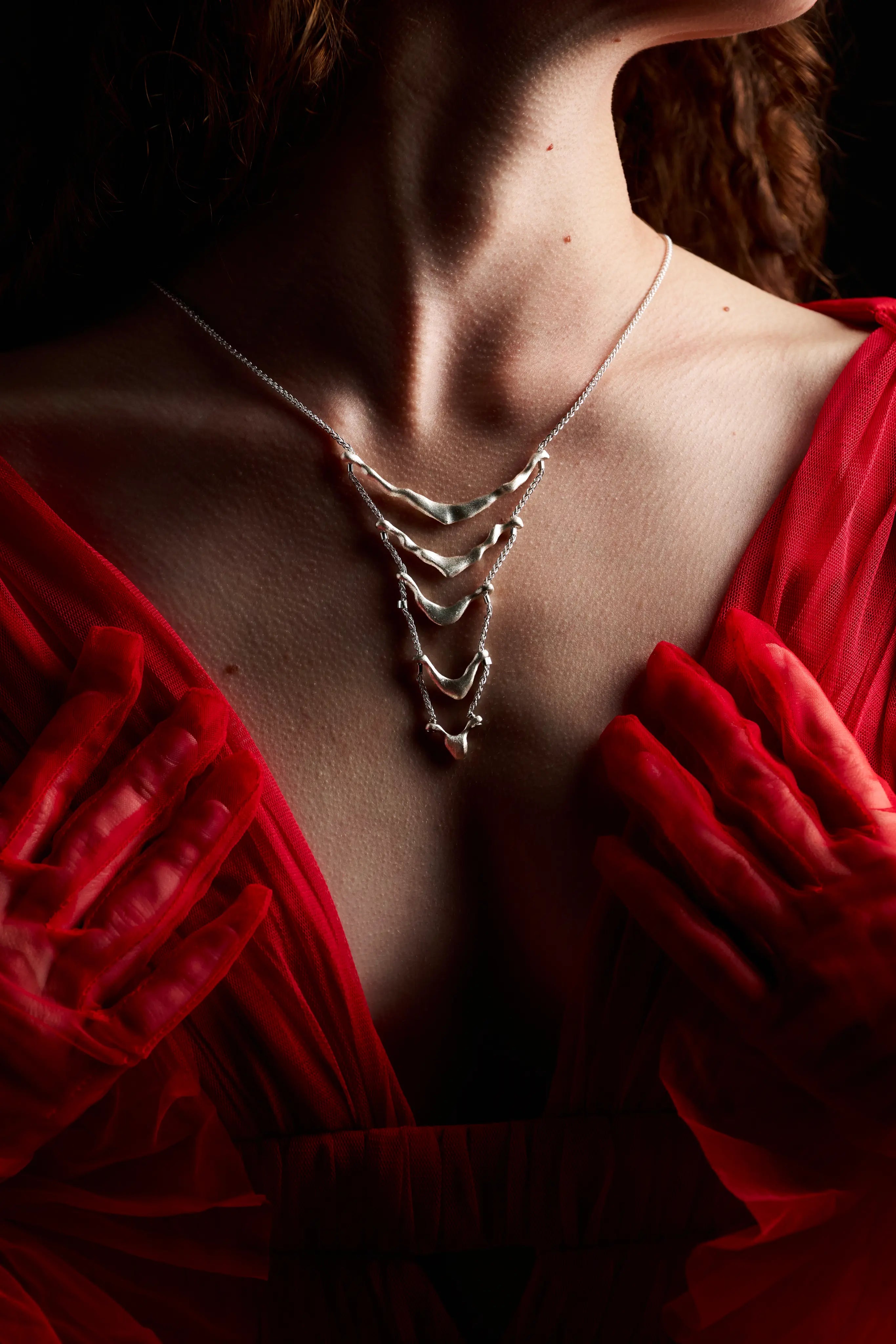 Femme portant le collier de dos Exo en argent visible sur le décolleté rouge.