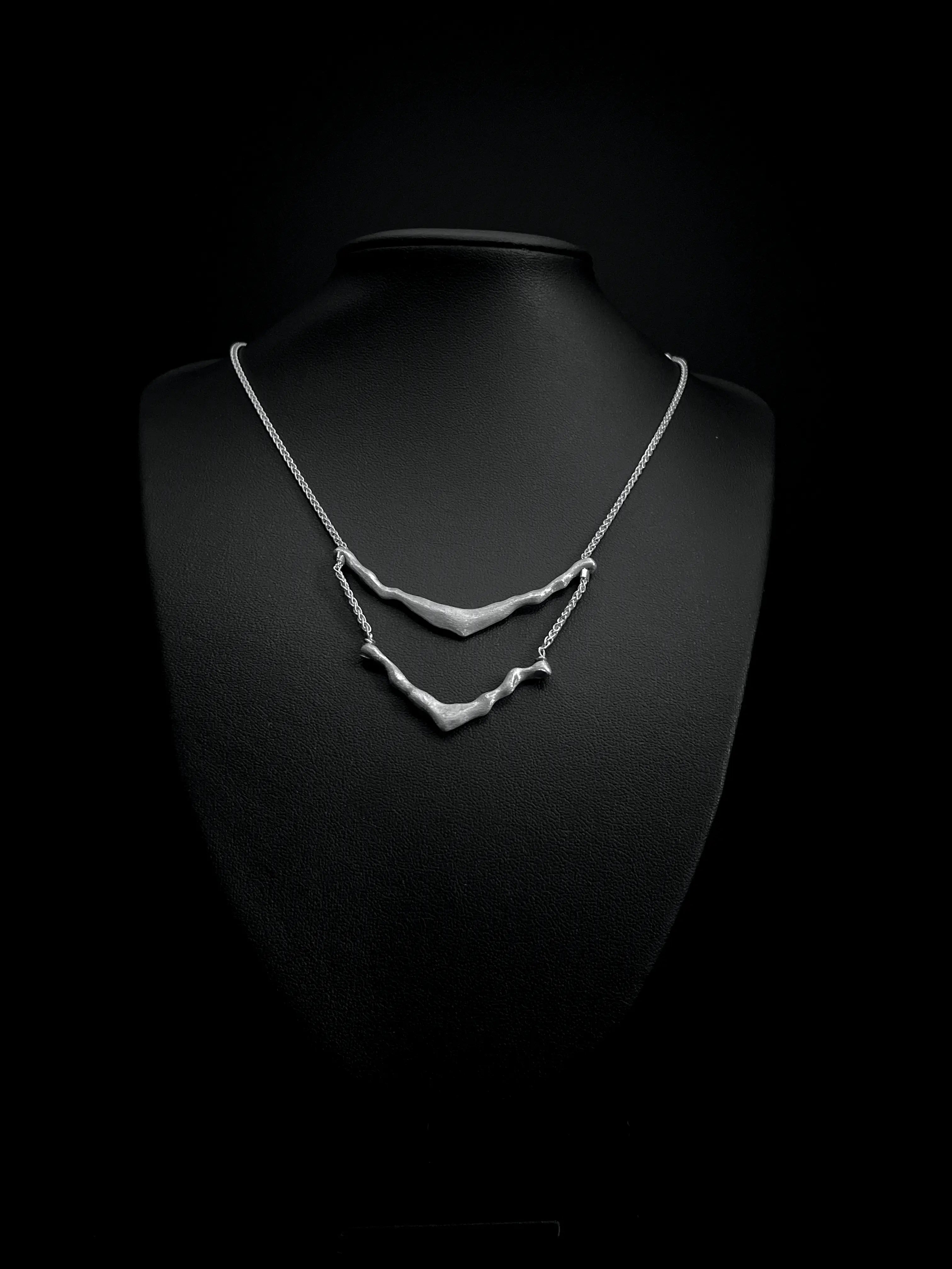 Vue de face du pendentif du collier de dos Exo en argent 925 sur fond noir.