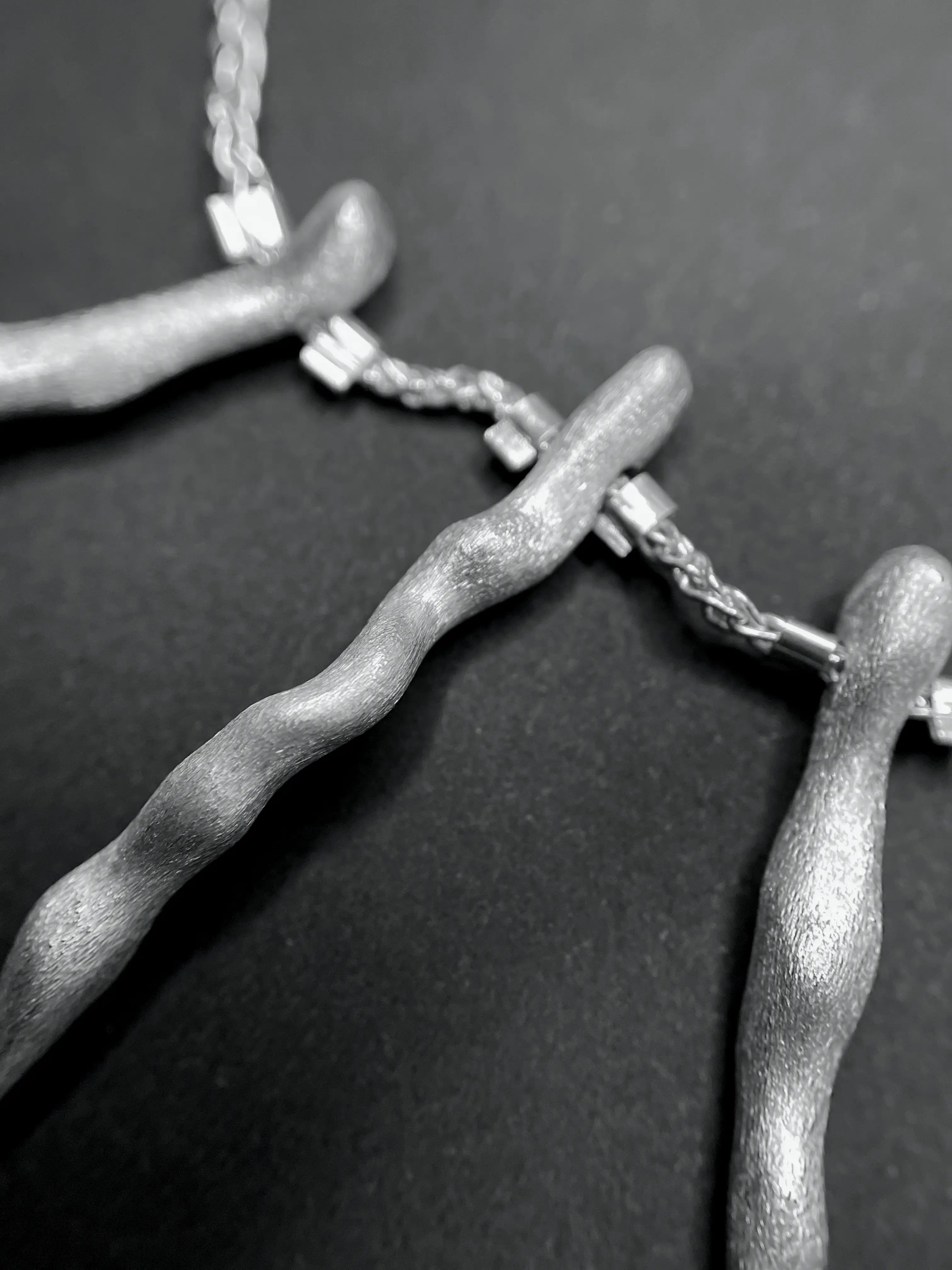 Macro du pendentif du collier de dos Osso en argent, montrant la texture et les perles d'argent.