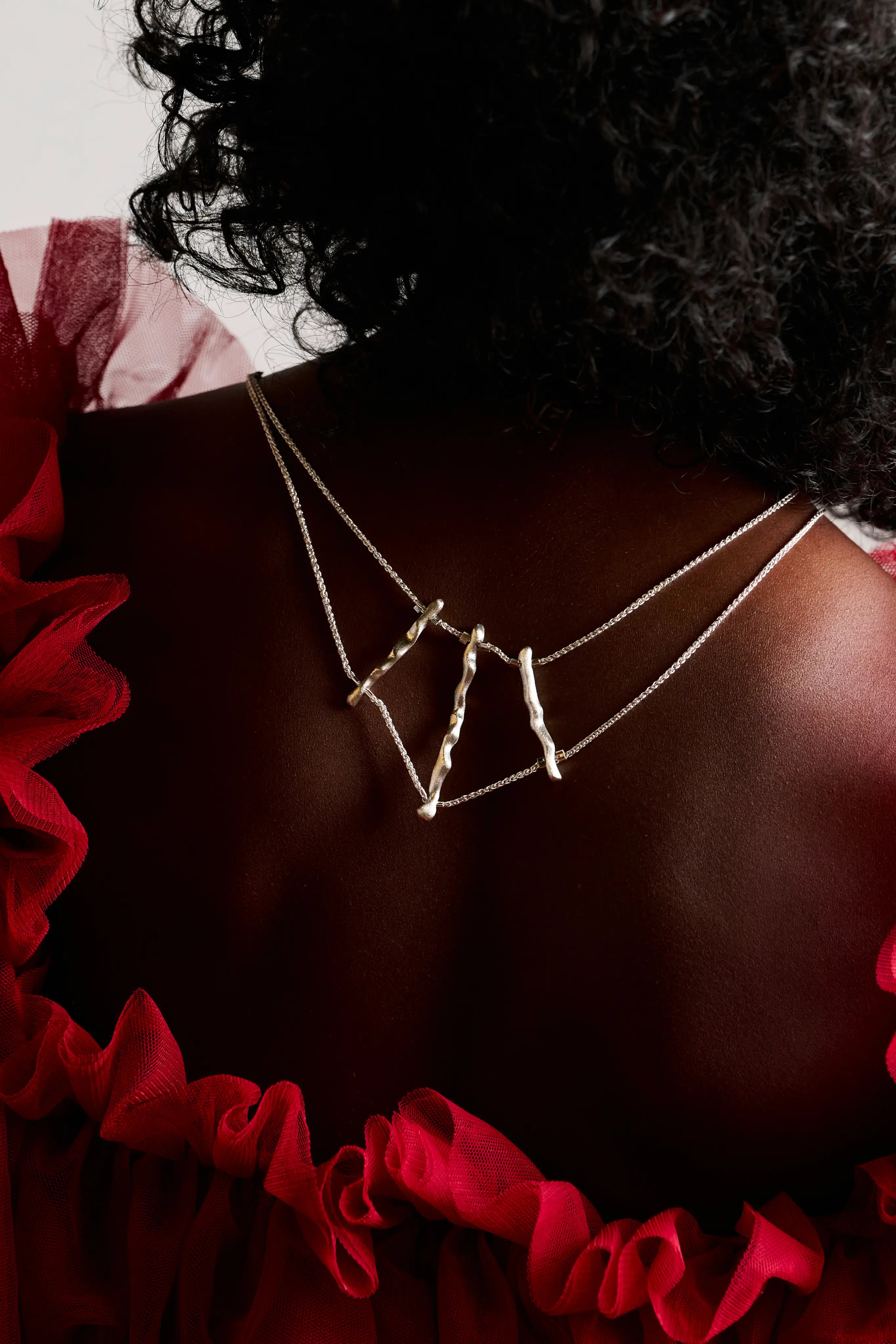 Gros plan sur le dos d'une femme portant le collier de dos Osso en argent 925 sous une robe rouge.