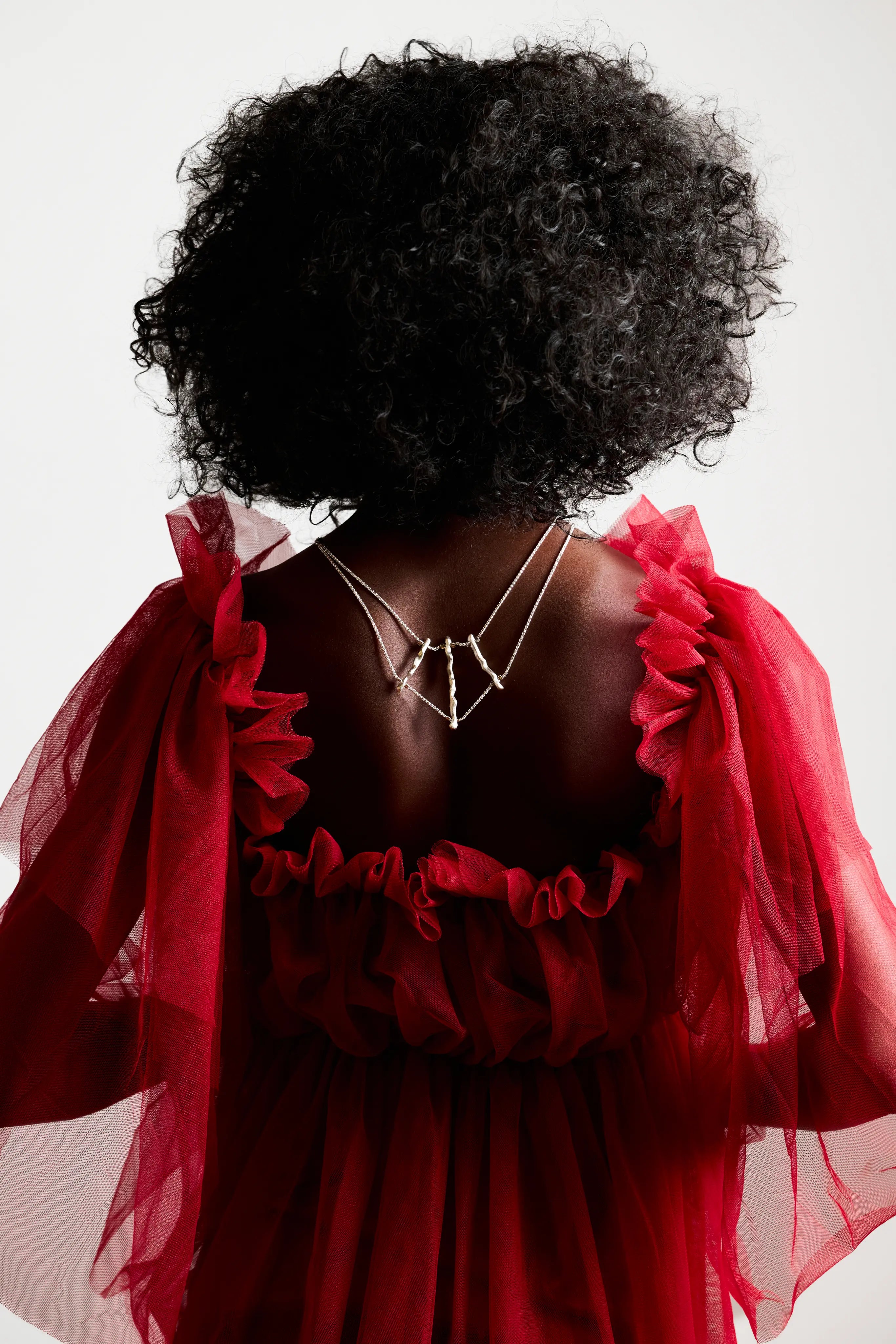 Femme de dos, en robe rouge, portant le collier de dos Osso en argent 925. Bijou fait main éthique.