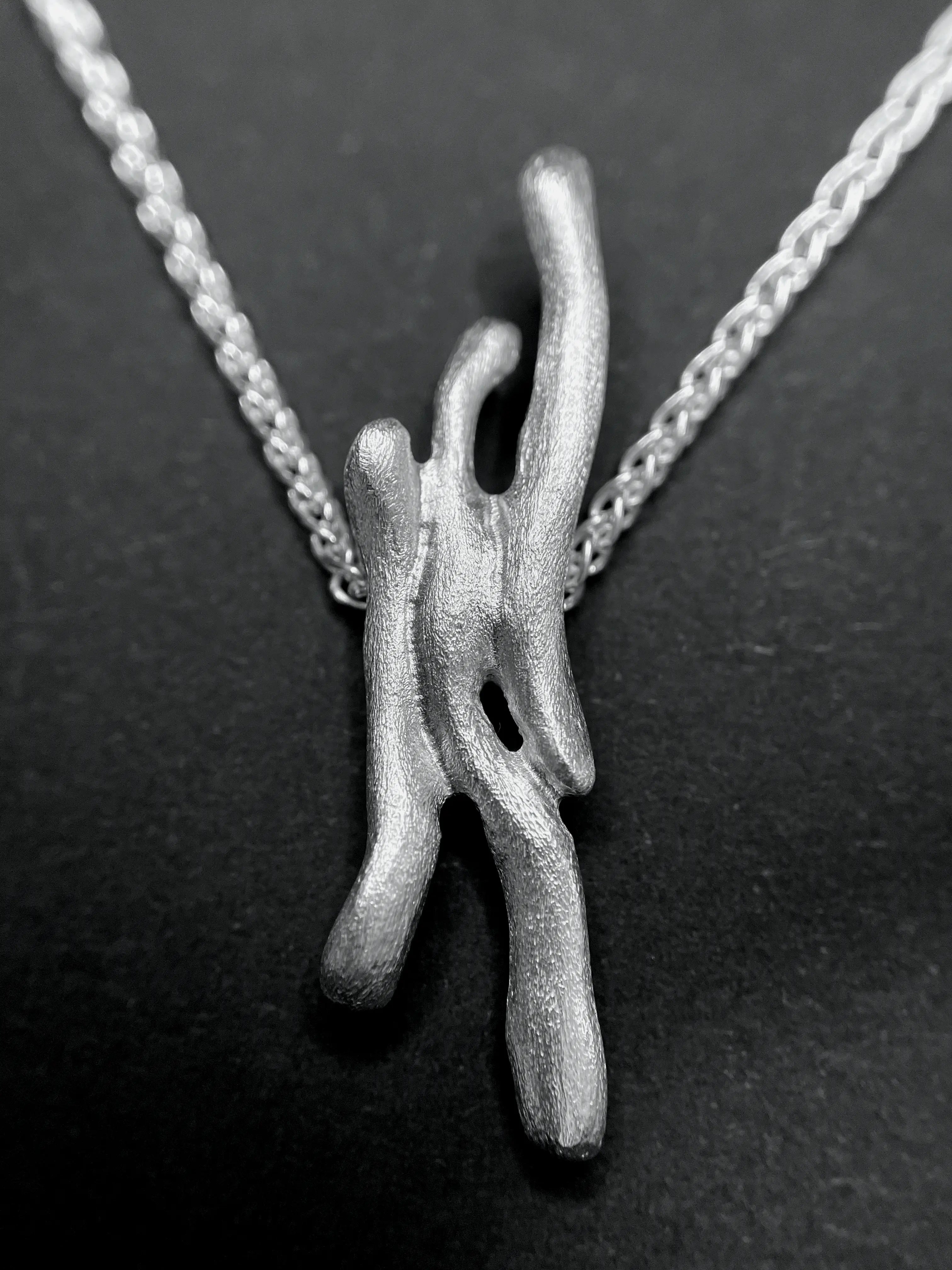 Macro du pendentif Dusa en argent, montrant la sculpture et la texture du travail fait main.