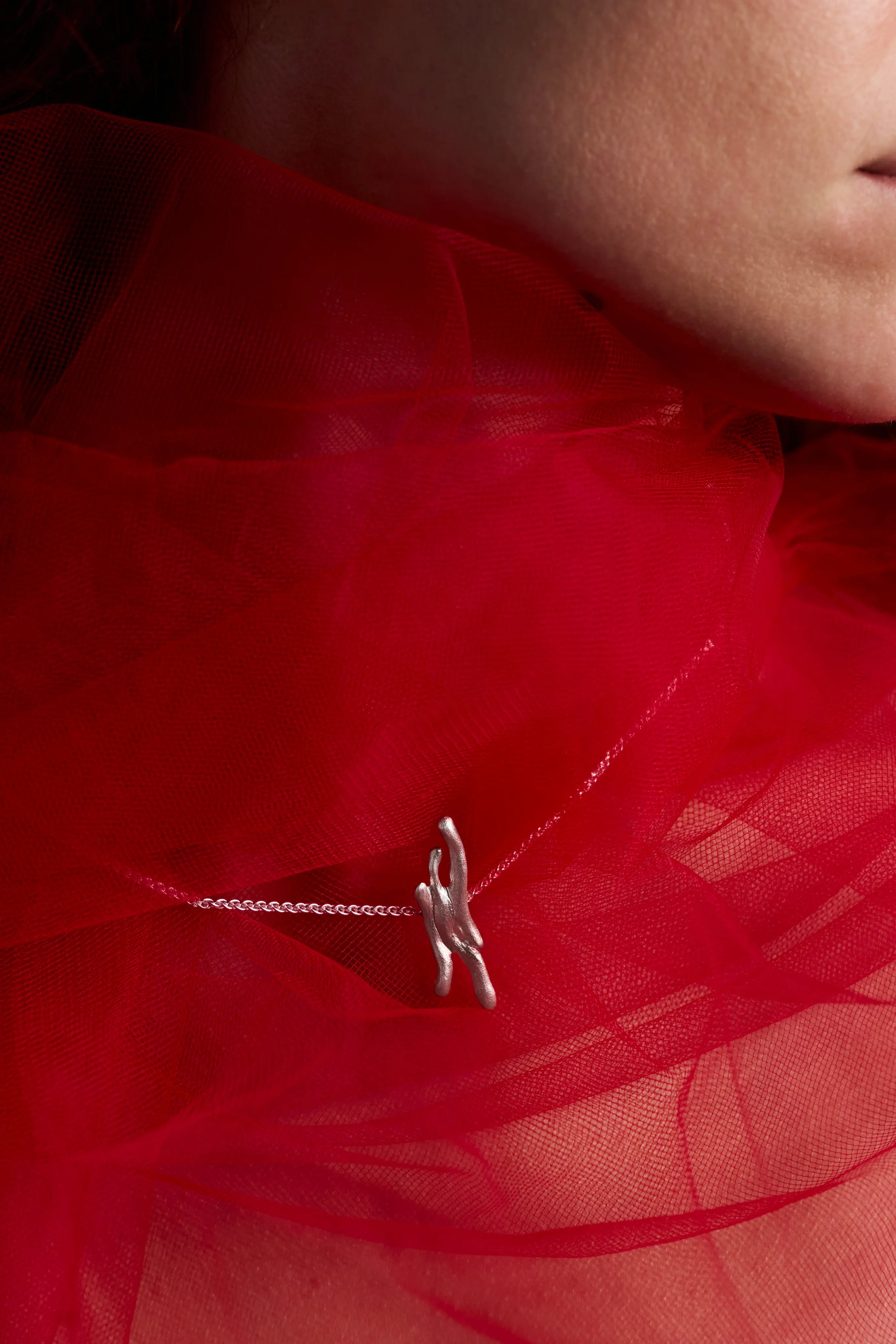 Gros plan sur le pendentif Dusa et les perles d'argent sculptées sur un fond rouge. Bijou artisanal de la collection Corail.