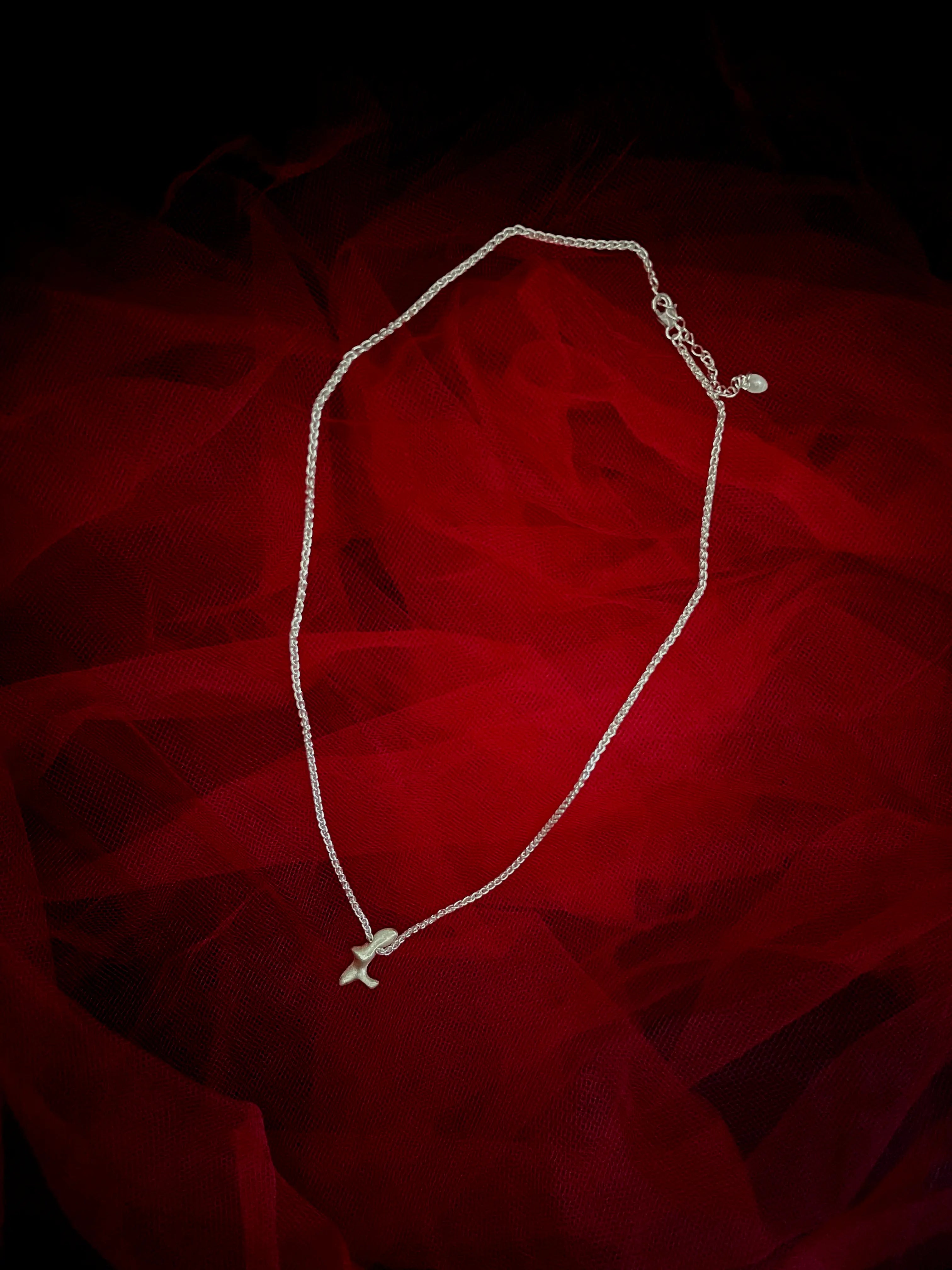 Collier Skel Synonys en argent 925 avec pendentif abstrait, sur fond de tissu rouge. Bijou fait main, collection Corail éthique.